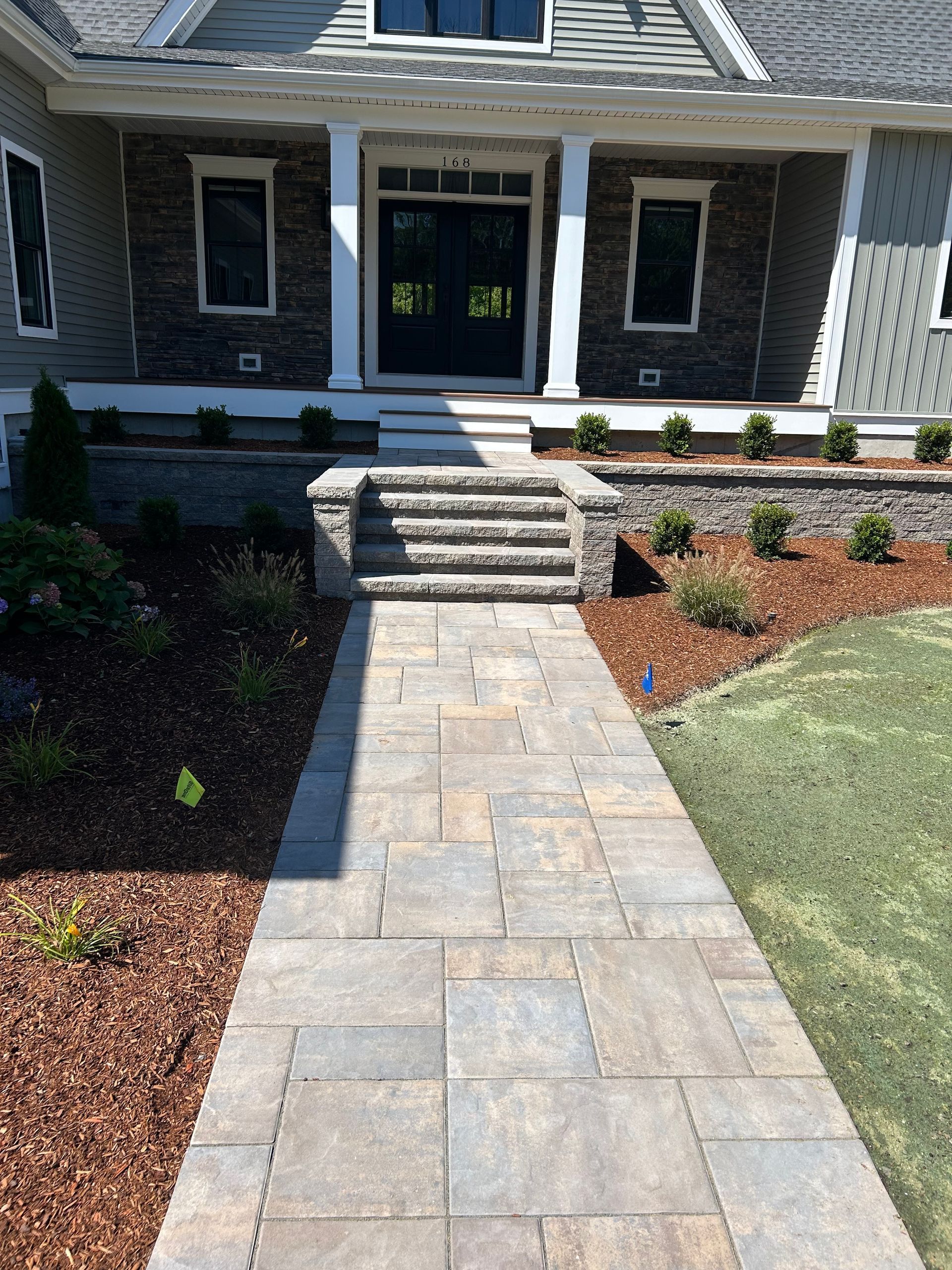 Stone walkway leading to a front porch with steps, dark door, and landscaped garden beds.
