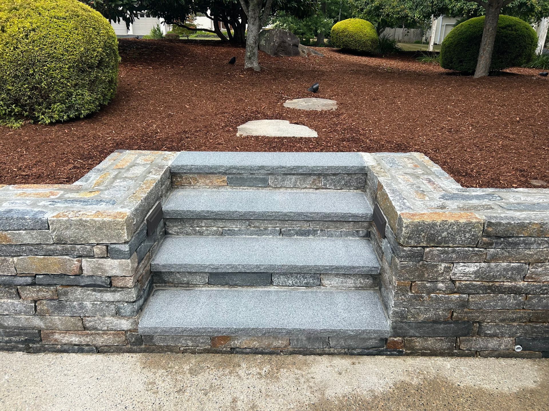 Stone steps in a landscaped garden with mulch, shrubs, and stepping stones leading upward