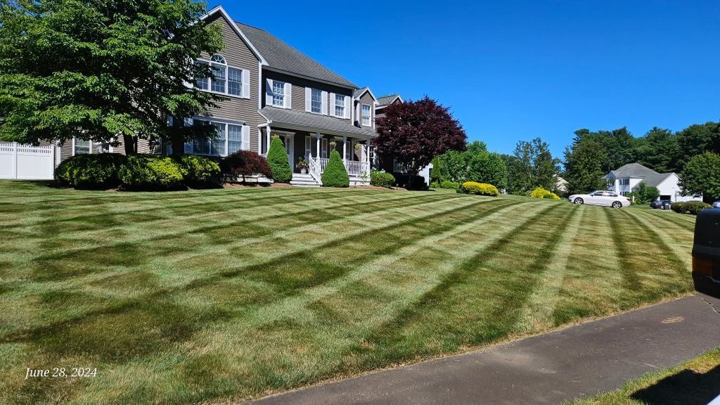 Suburban house with manicured striped lawn on a sunny day, viewed from the sidewalk