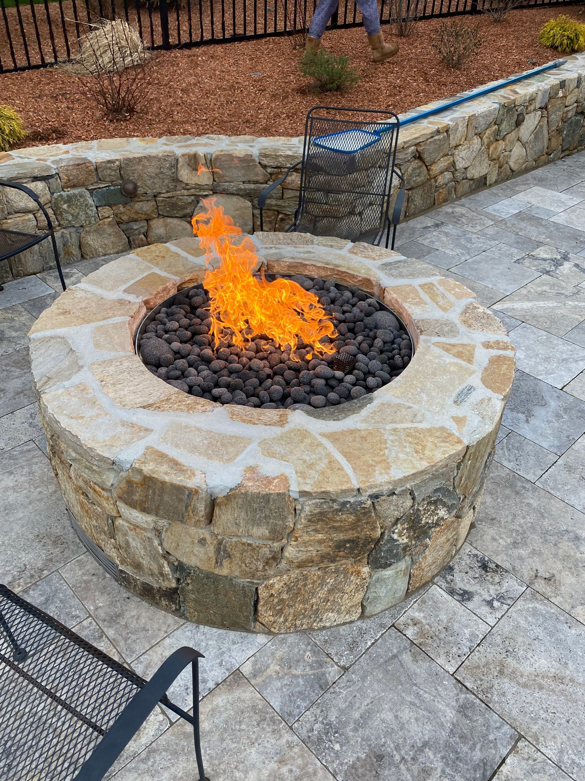 A fire pit is sitting on a patio next to a stone wall.