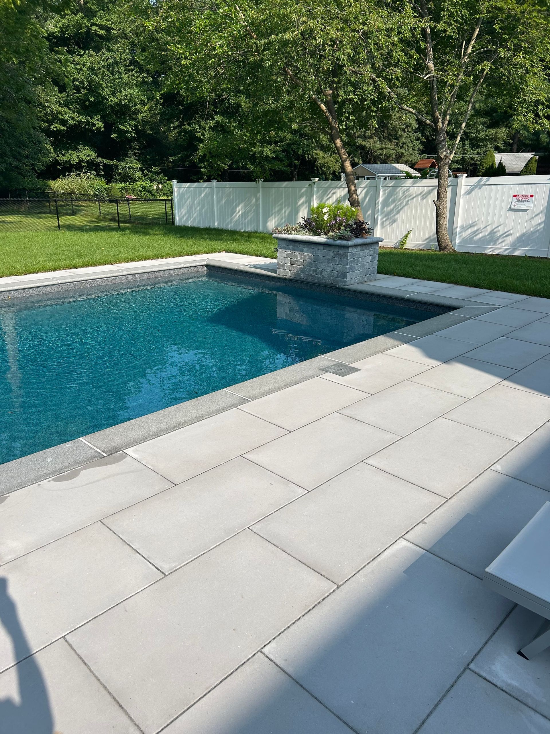 There is a large swimming pool in the backyard with a white fence.