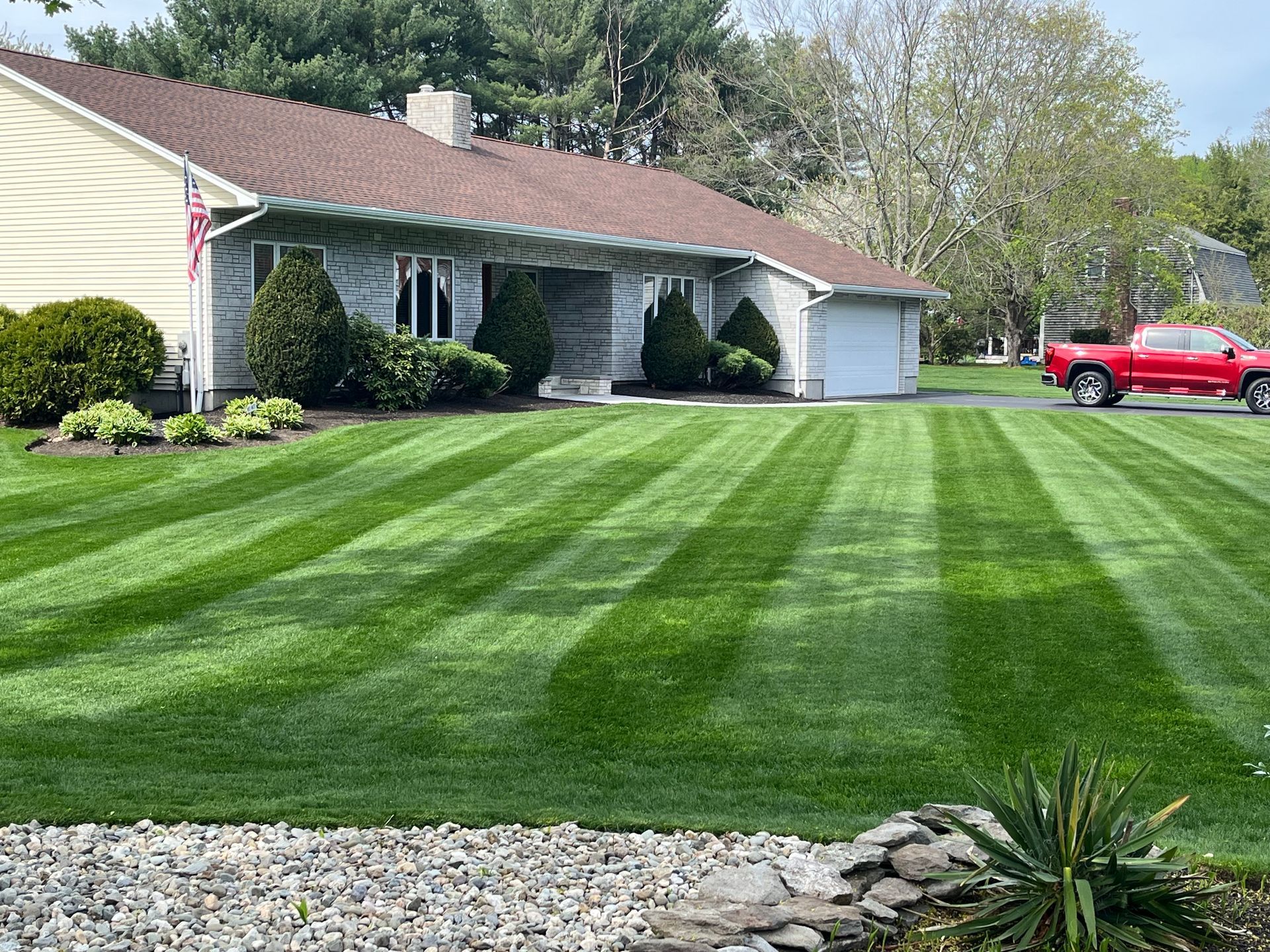 A red truck is parked in front of a house with a lush green lawn.