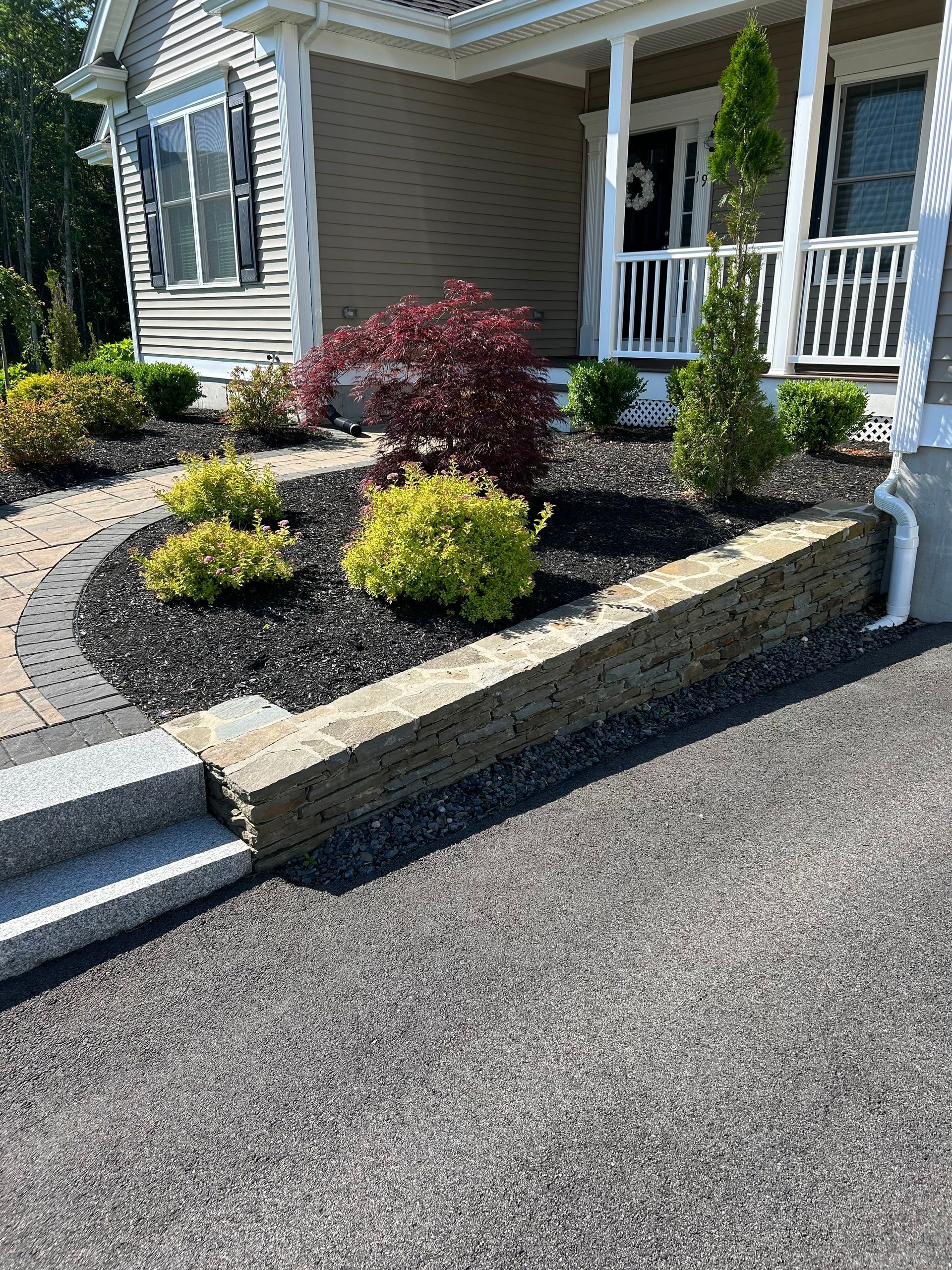 A house with a porch and a stone wall in front of it.