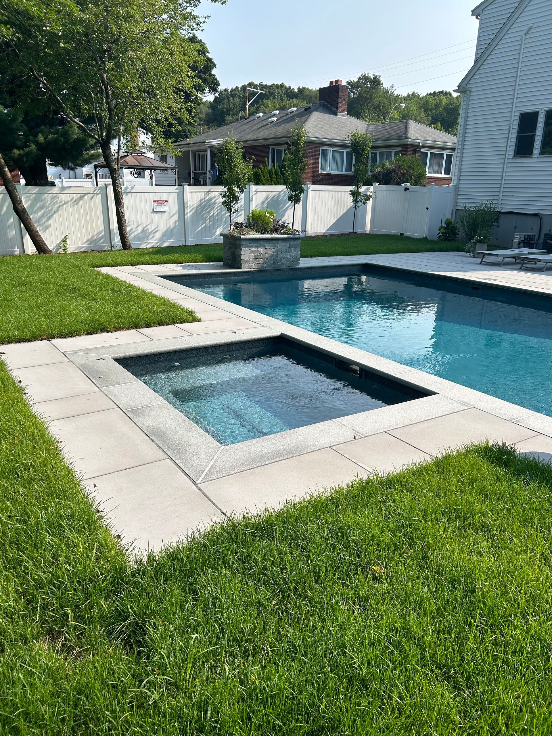 A large swimming pool with a hot tub in the backyard of a house.