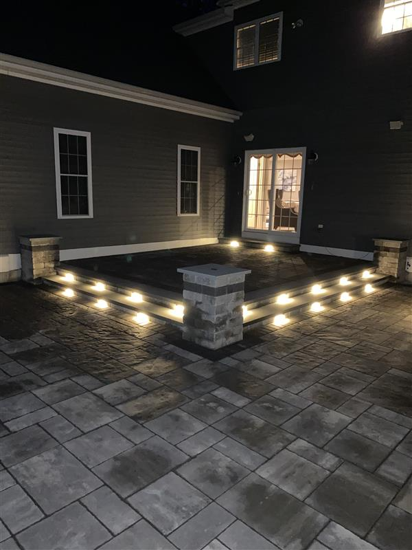 Night view of a brick patio with steps and glowing lights, leading to a house entrance.