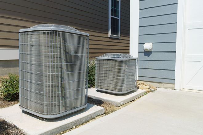 Two outdoor air conditioning units beside a house wall and white door