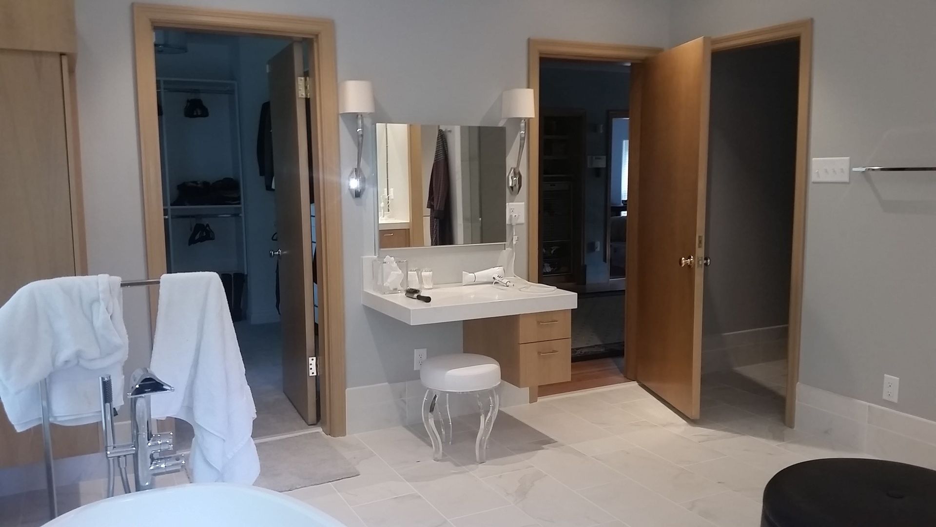 A bathroom with a tub , vanity , mirror and stool.