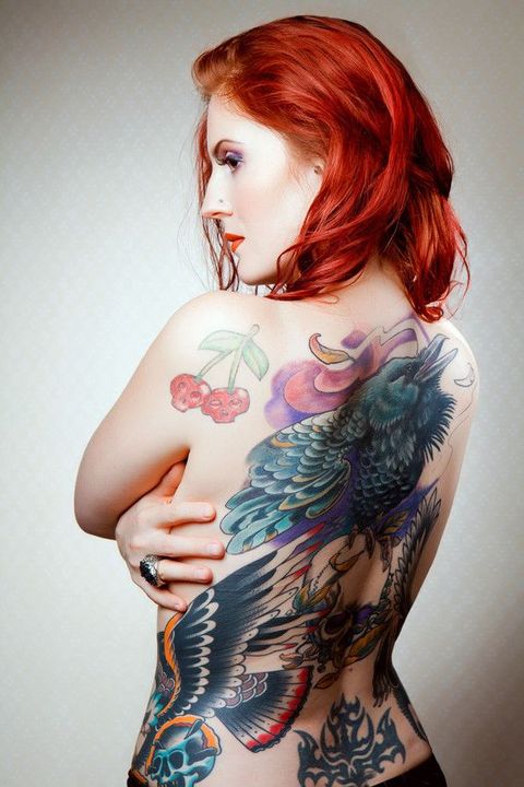 A woman with red hair has a lot of tattoos on her back.