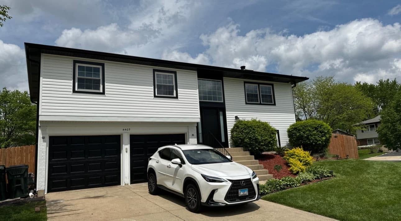 Two-story white house with black garage doors and a white car parked in the driveway.