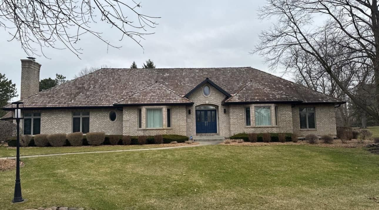 Single-story brick house with a tiled roof, blue front door, and leafless trees in a grassy yard.