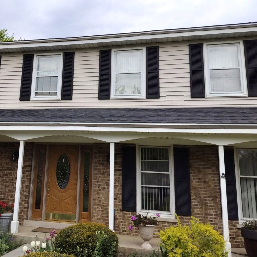 Two-story brick and siding house with black shutters, front porch, and potted flowers