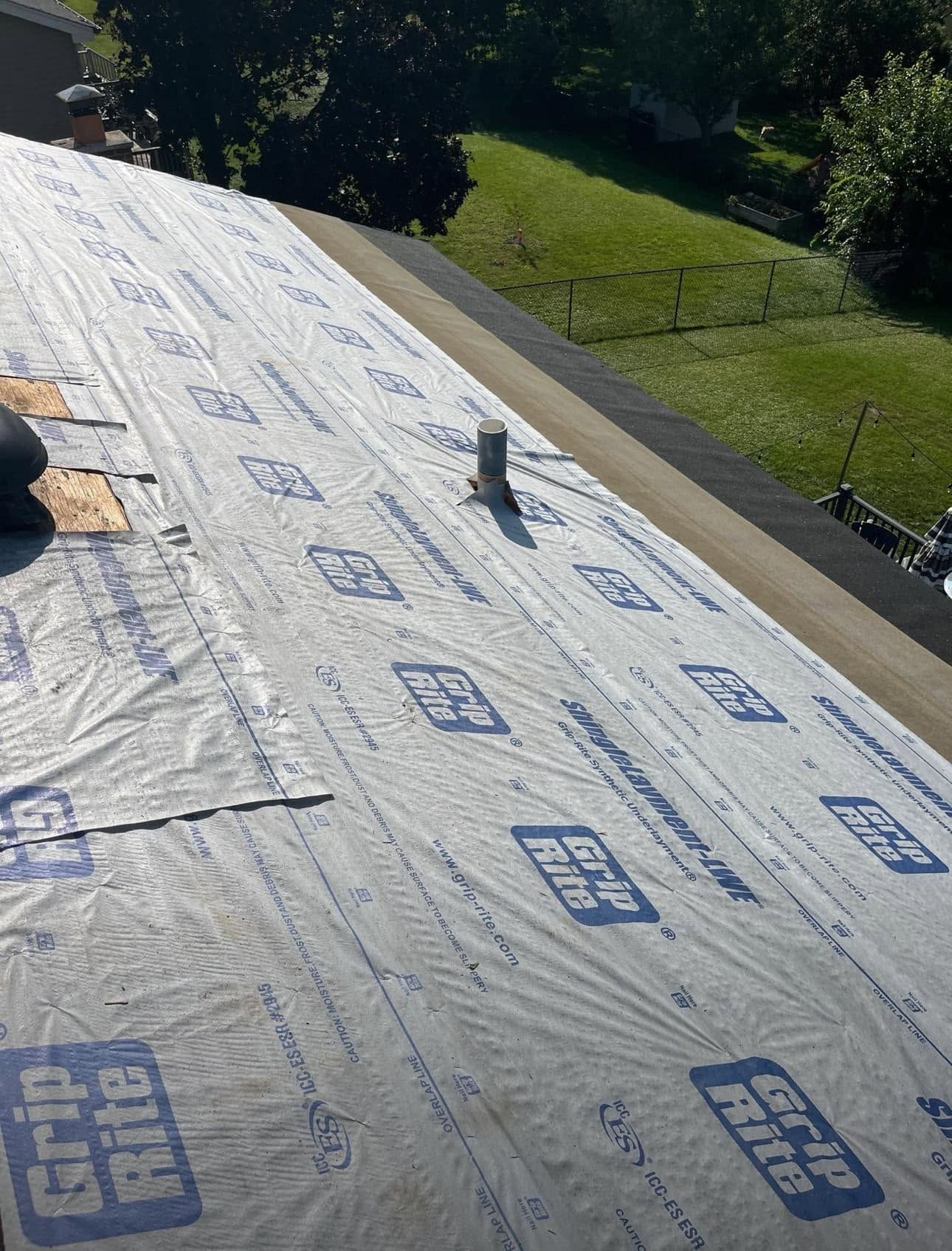 Roof underlayment being installed on a sloped roof with a vent pipe and grassy yard below