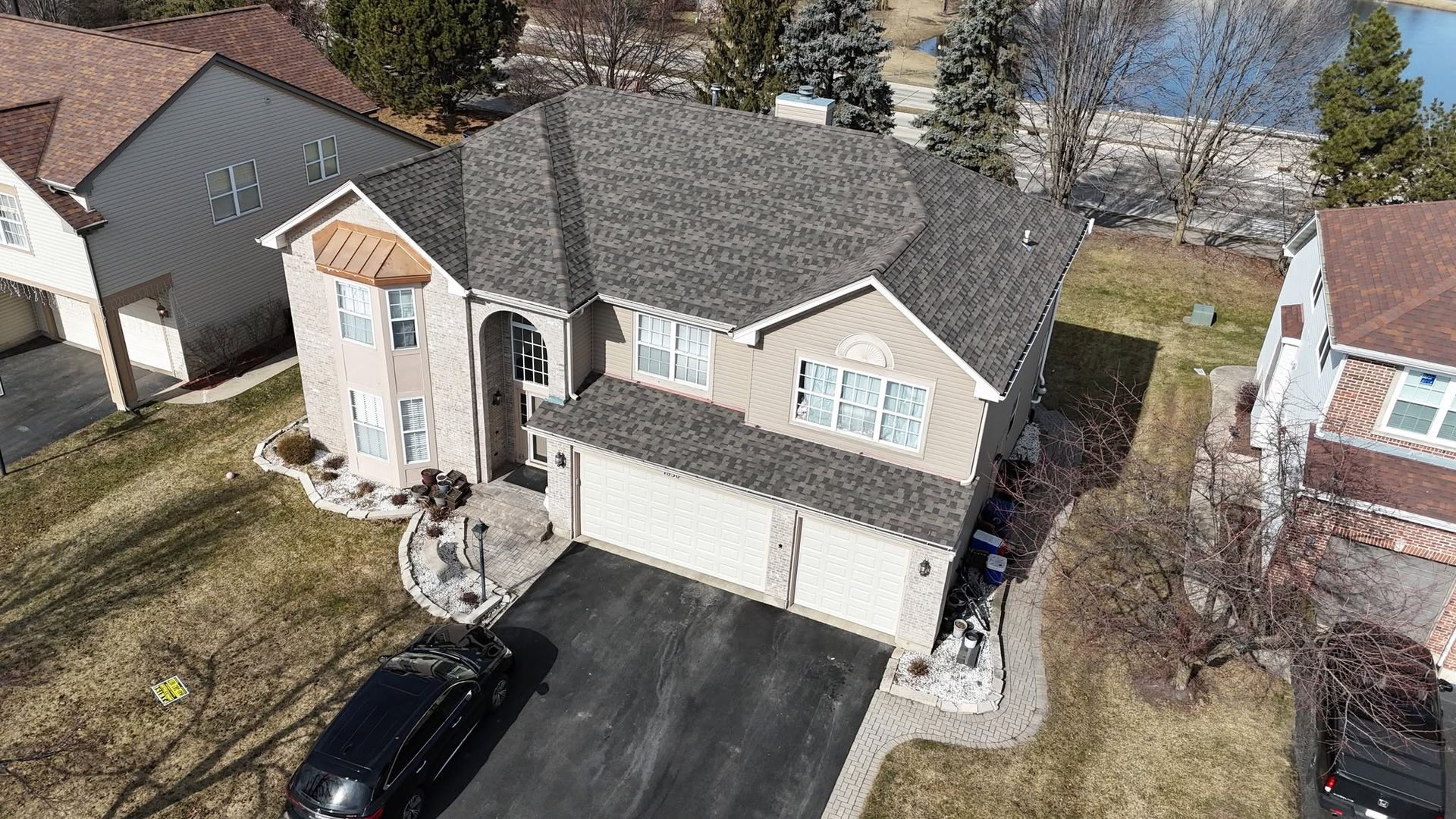 Aerial view of a two-story suburban house with a black driveway, garage, and a parked car.