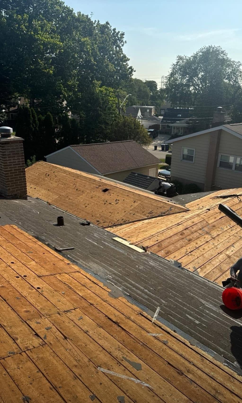 Rooftop under renovation with exposed plywood, tar paper seams, and trees and houses in the background
