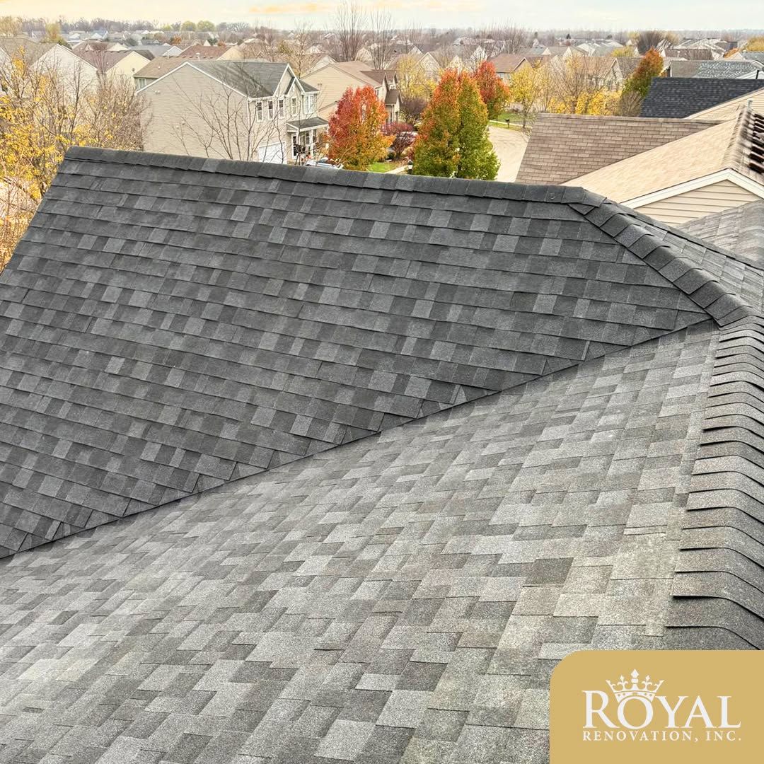 Roofing shingles on a steep house roof, with autumn trees and neighboring homes in the background.