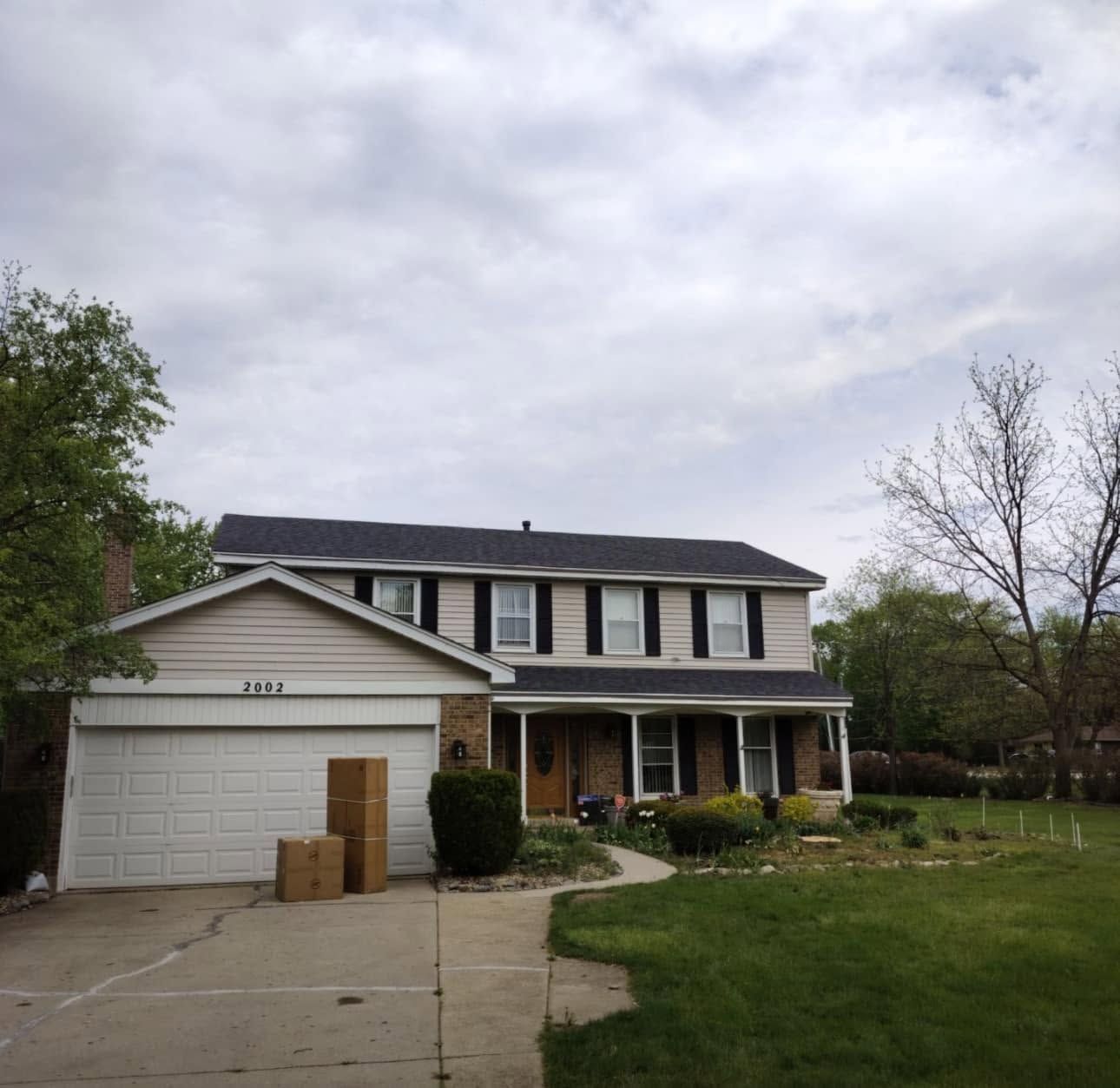 Suburban two-story house with a garage and boxes on the driveway under a cloudy sky