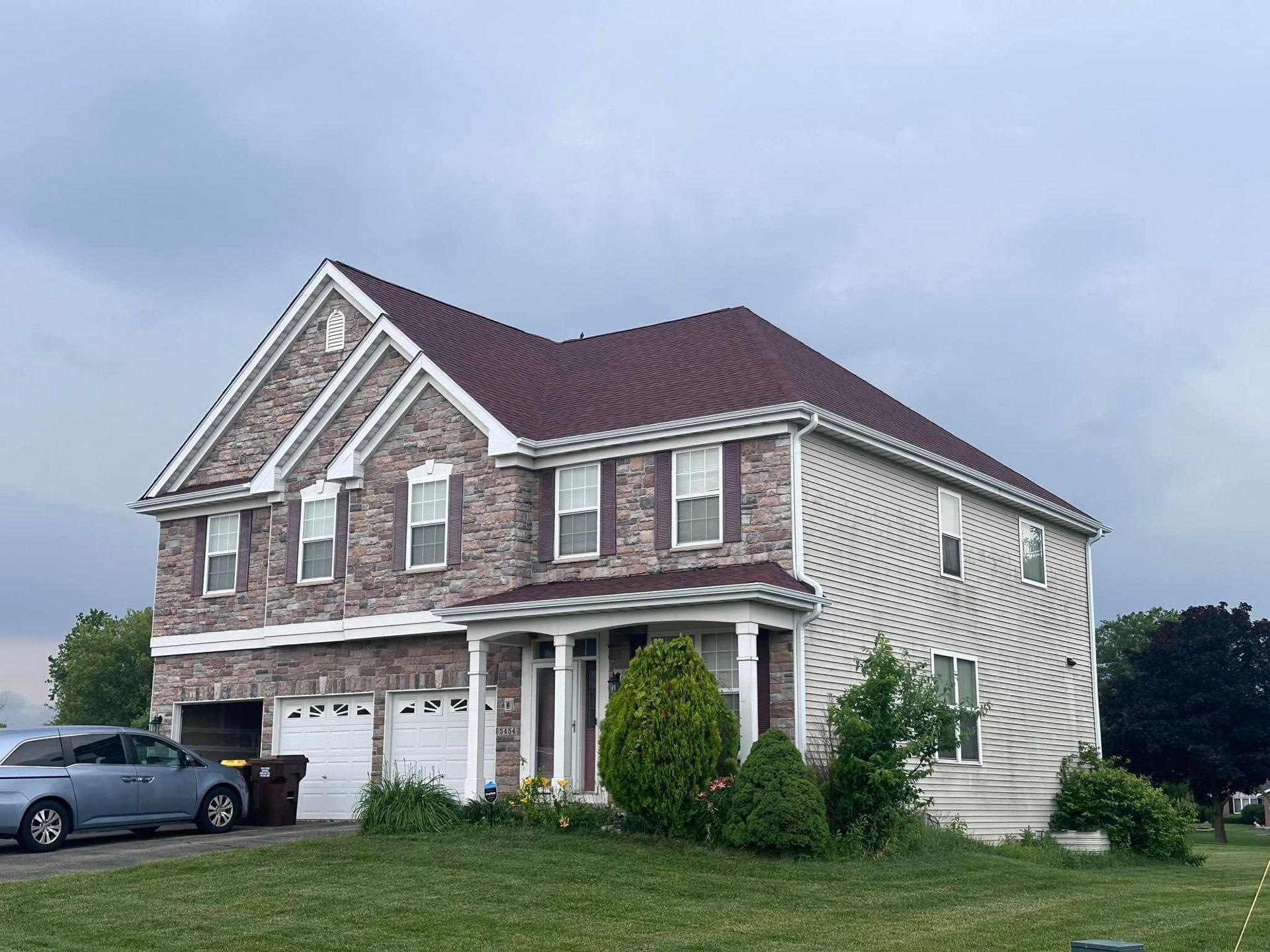 Two-story brick house with white trim, a garage, and a parked car under a cloudy sky