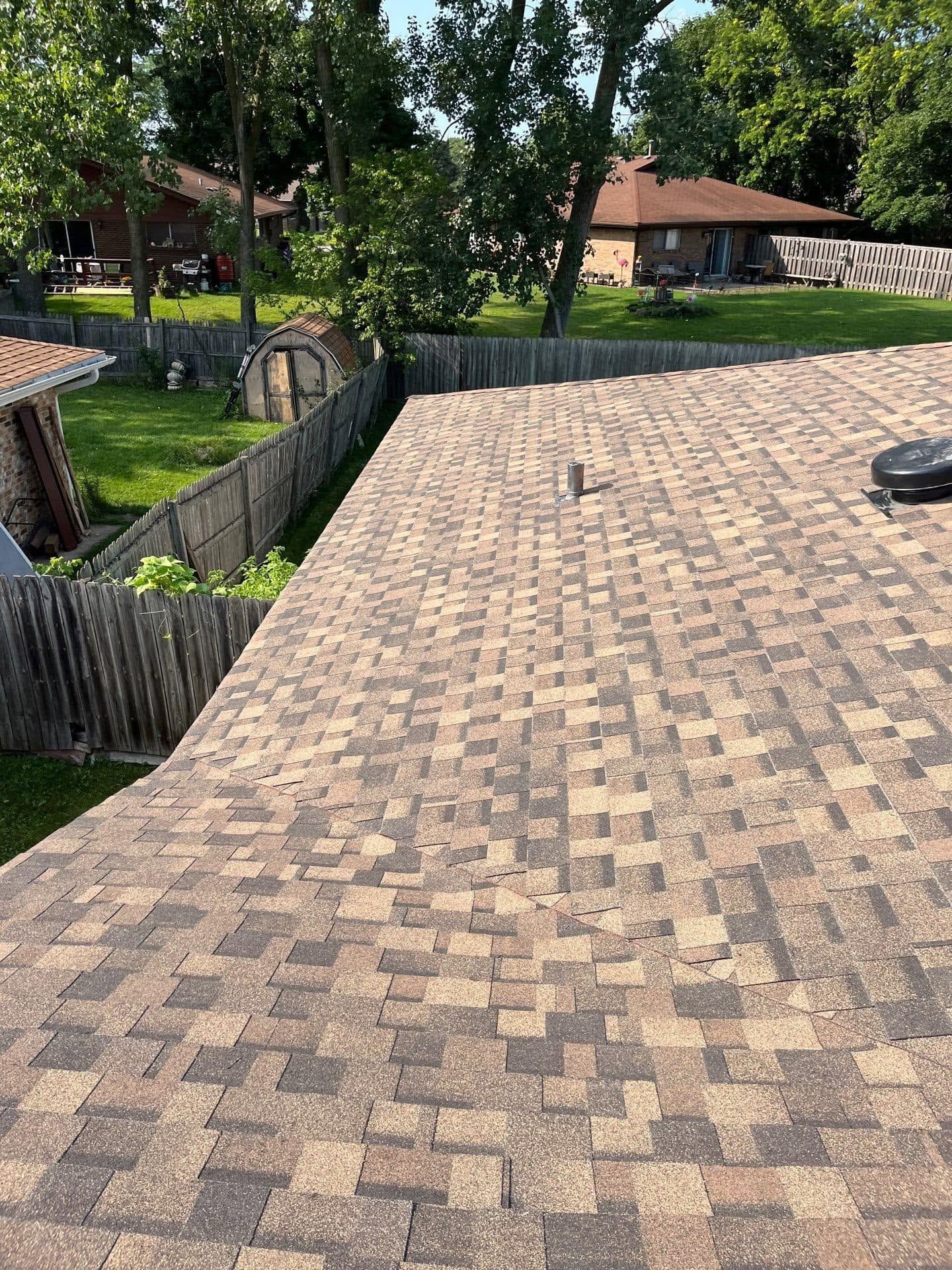 Tan shingle roof with trees and a house in the background, seen from above.