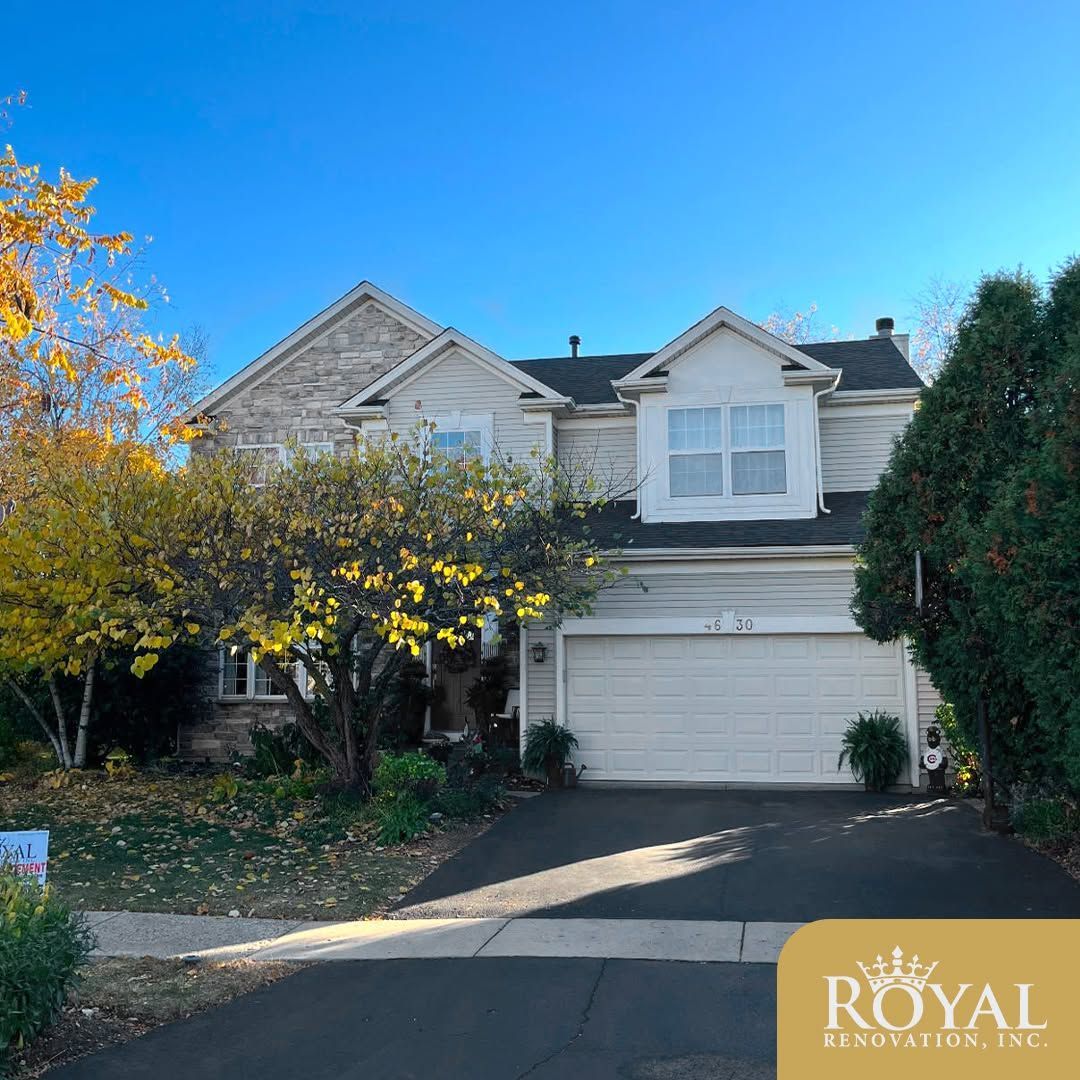 Suburban two-story house with white siding, garage, and autumn trees under a bright blue sky