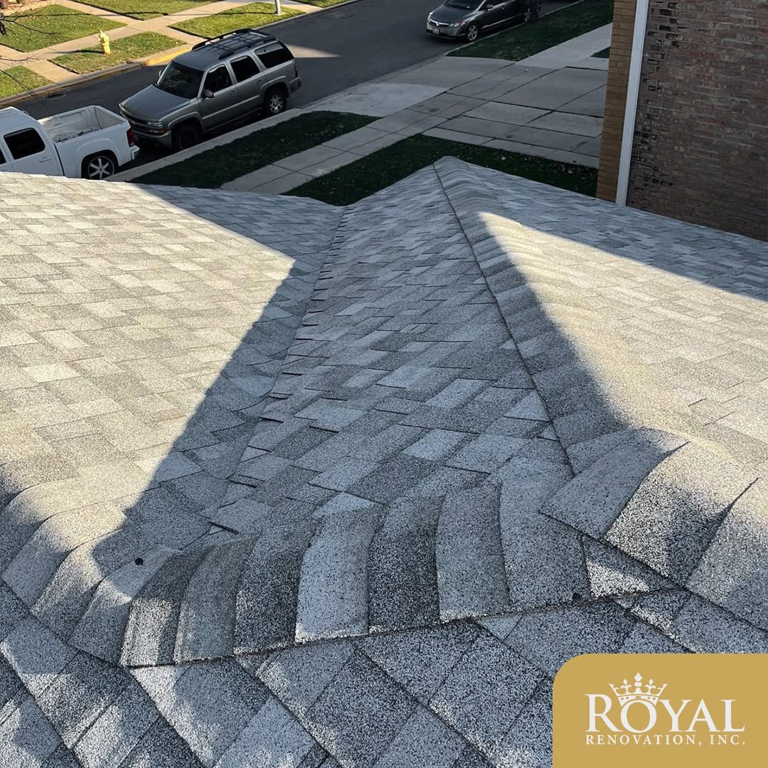 Gray shingled roof ridge on a suburban house, with parked vehicles and a lawn visible below.