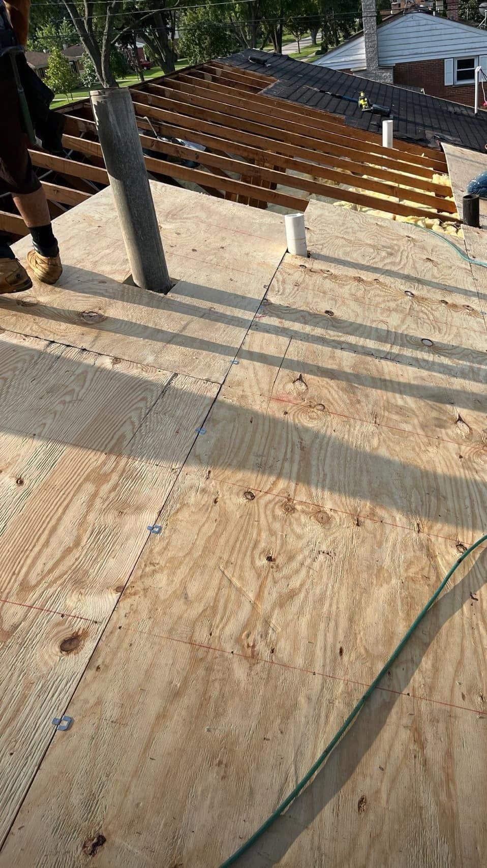 Wooden deck under construction with joists, concrete posts, and a worker’s shadow on plywood flooring.