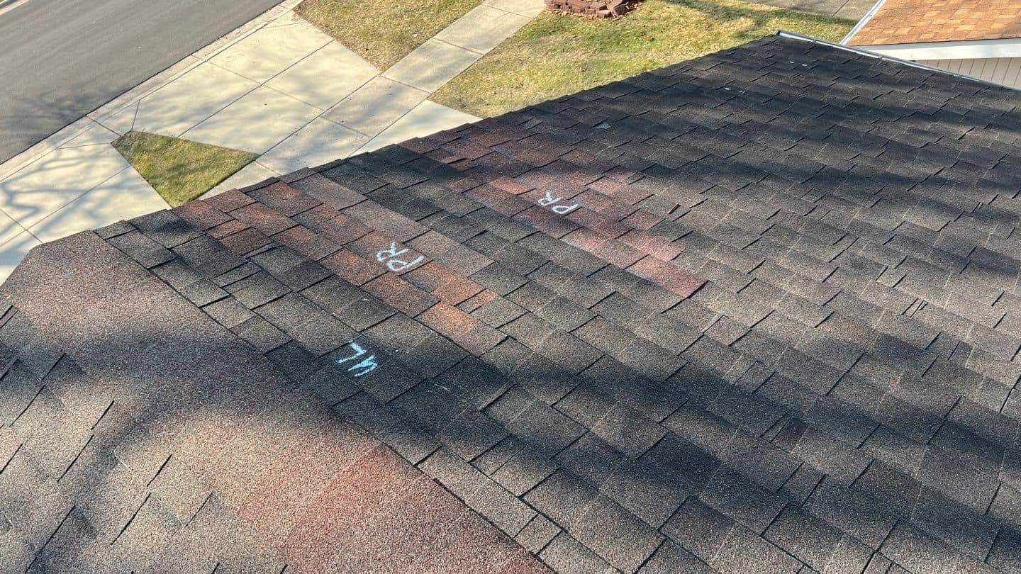 Rooftop shingles with scattered chalk marks and tree shadows beside a concrete walkway