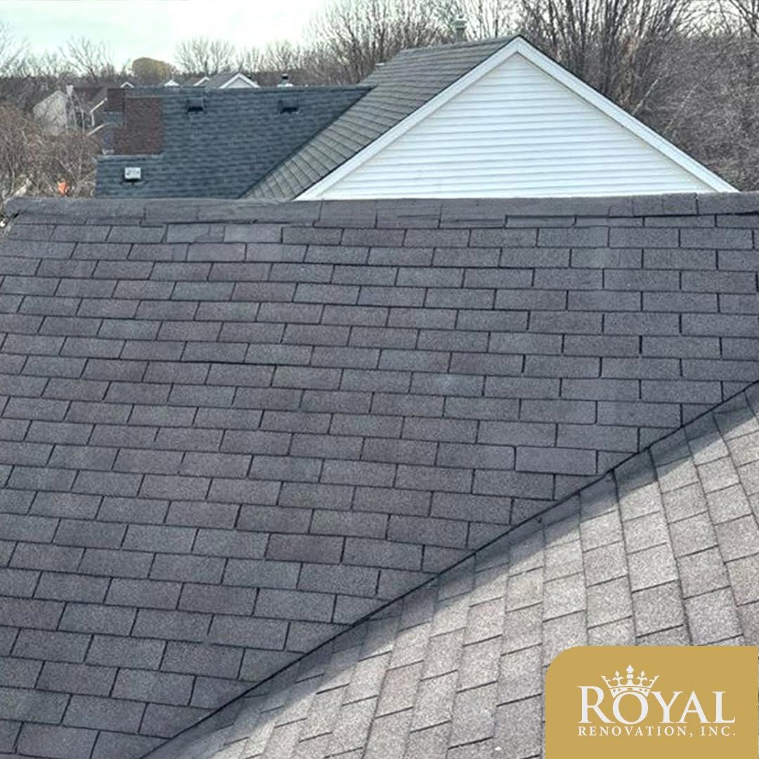 Two overlapping asphalt shingle roofs, dark gray and light gray, with a white gable in the background.