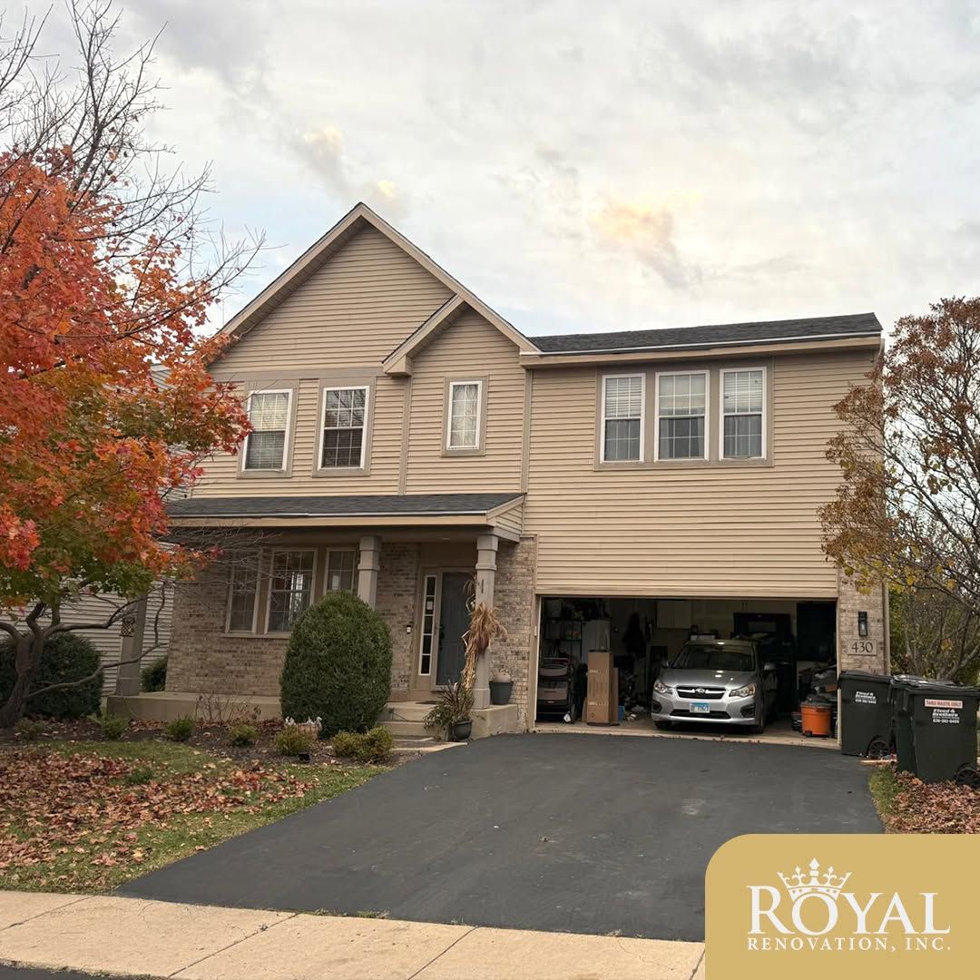 Two-story beige house with a driveway, garage, and autumn trees in front