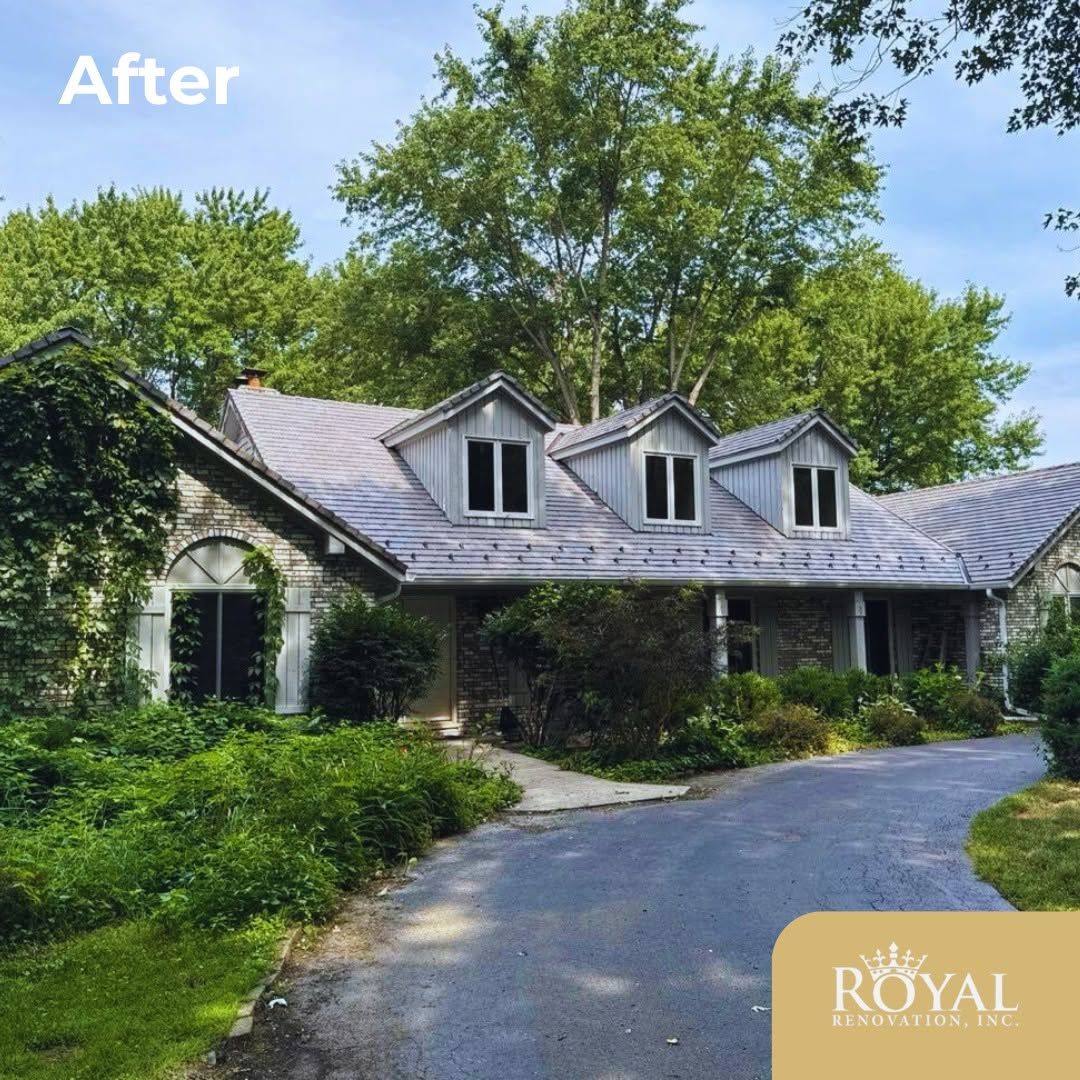 Curved driveway leading to a gray-roofed house surrounded by lush green trees and shrubs
