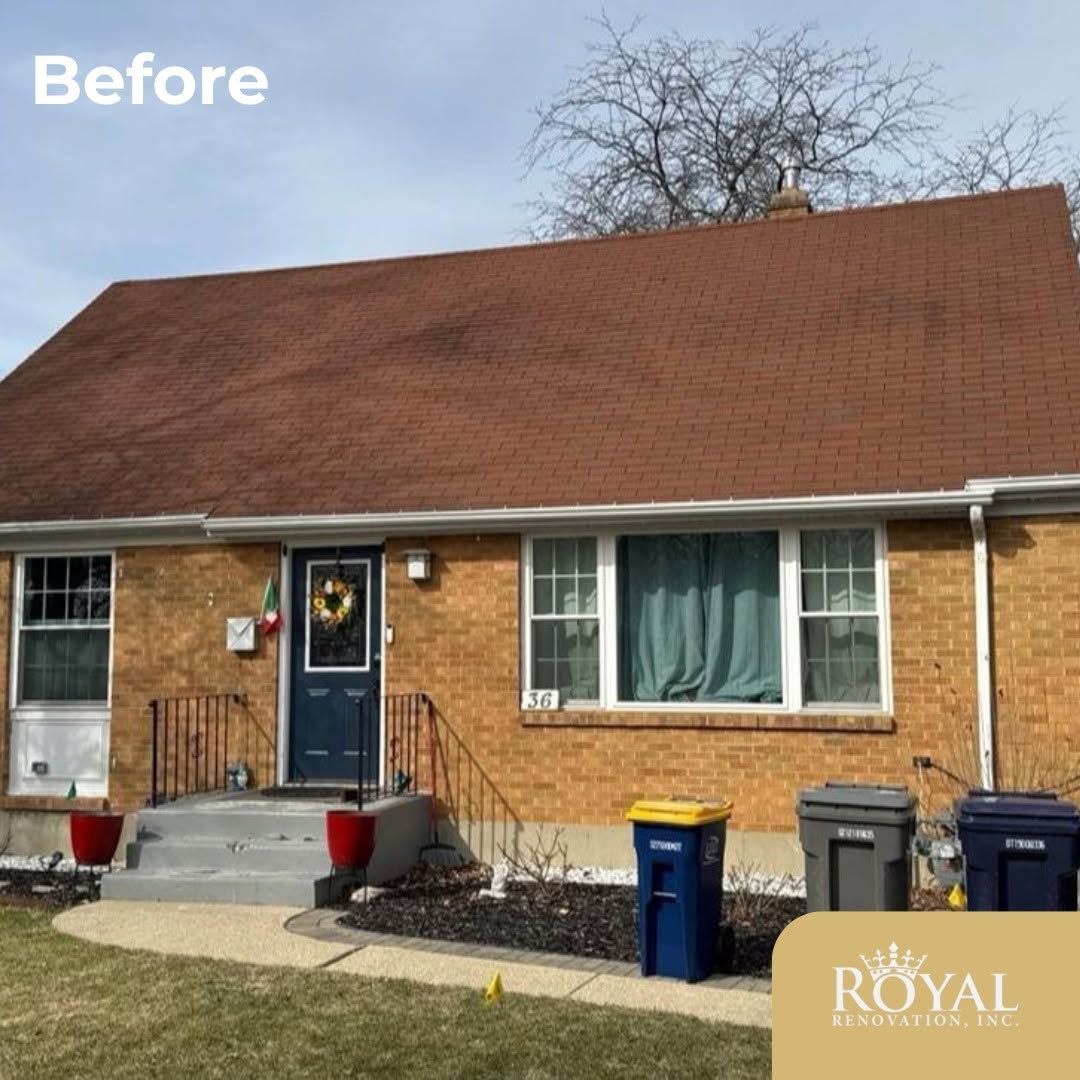 Front view of a brick house with a red roof, blue front door, and trash bins along the sidewalk.