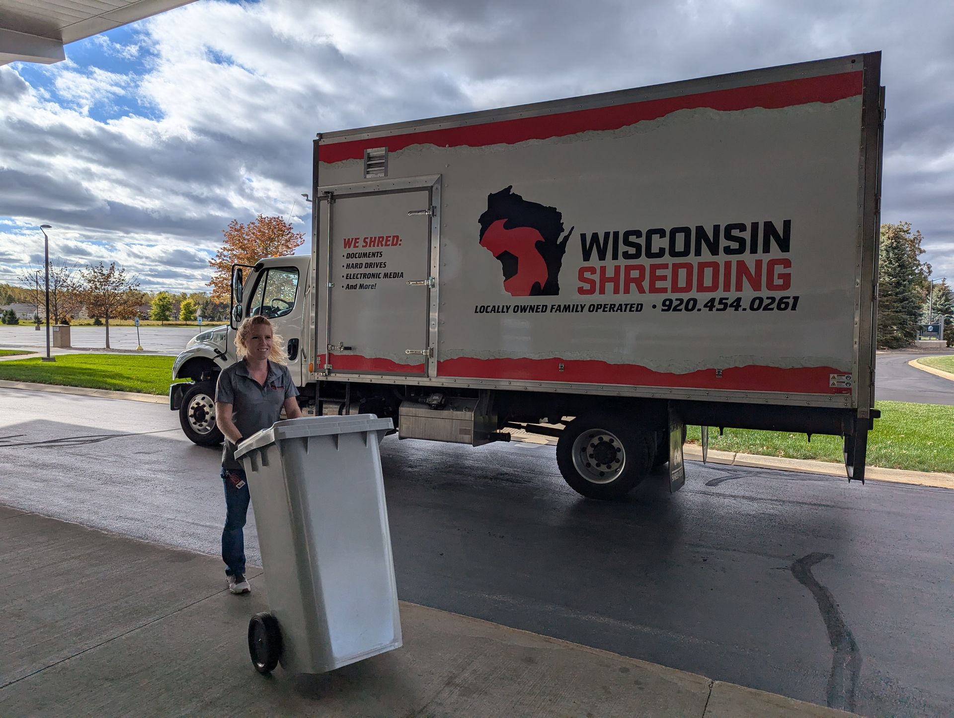 A woman is holding a trash can in front of a wisconsin shredding truck.