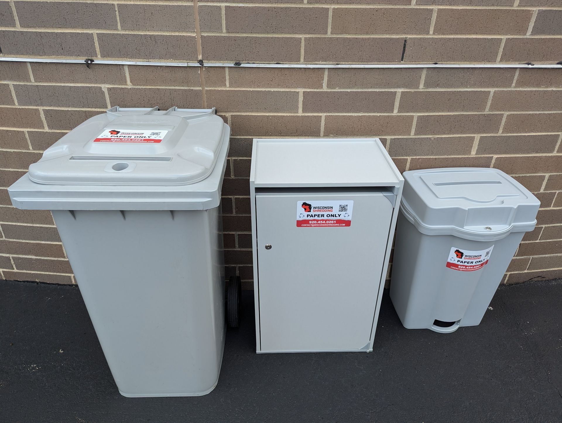 Three trash cans are lined up against a brick wall