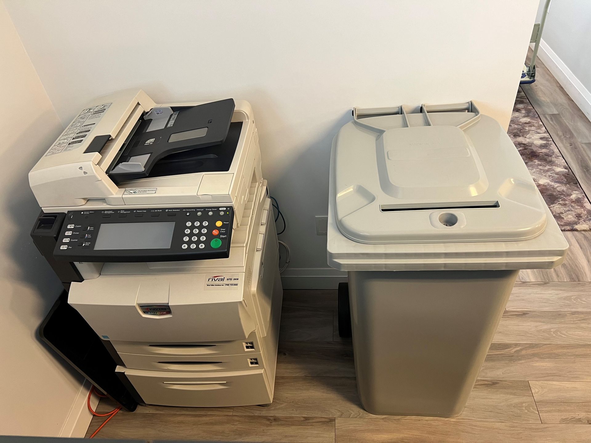 A printer and a trash can are sitting next to each other in a room.