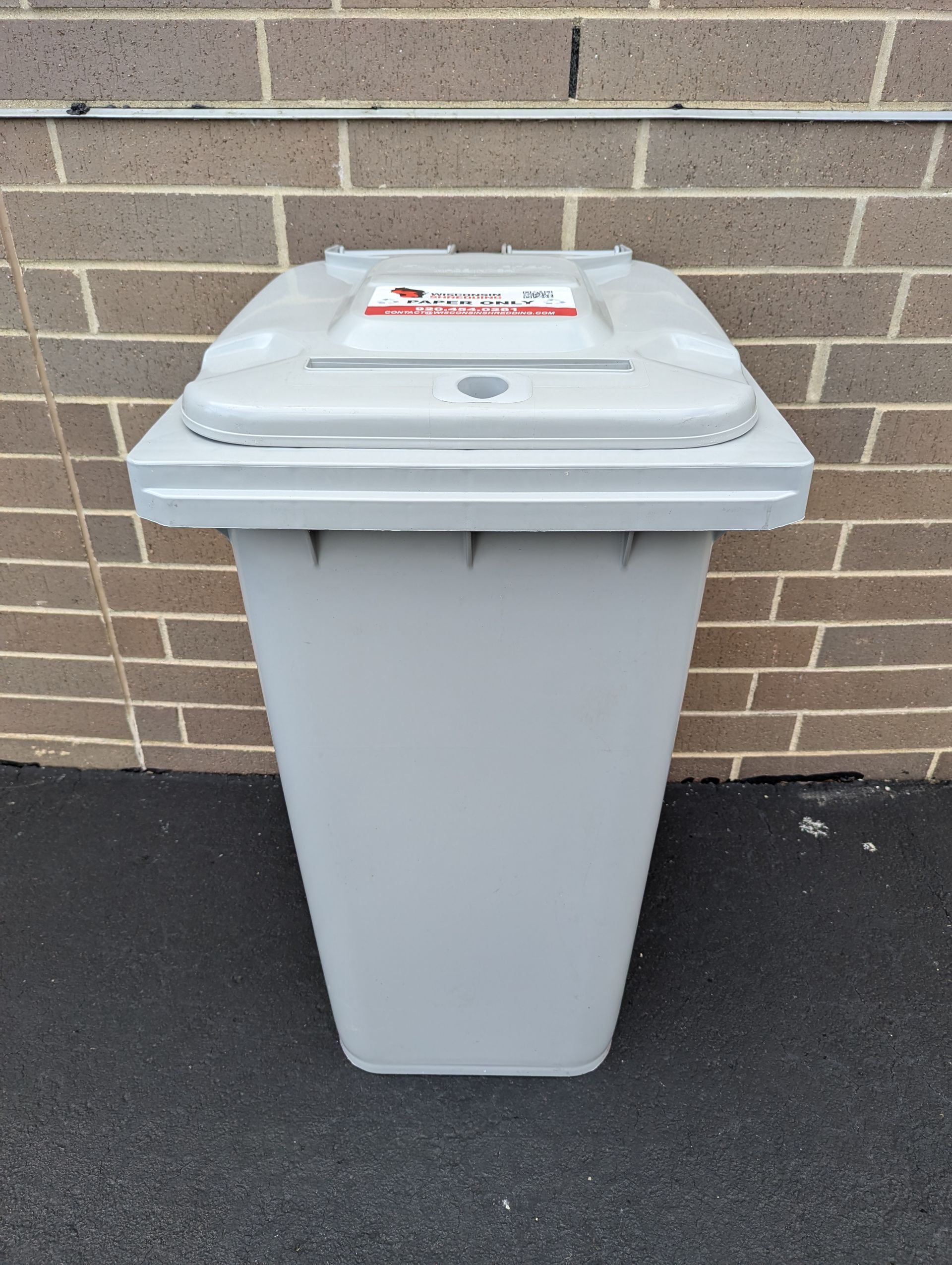 A grey trash can is sitting in front of a brick wall