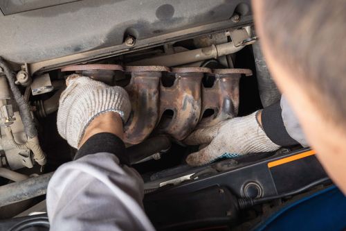 Gloved hands working under a car hood on the engine manifold.