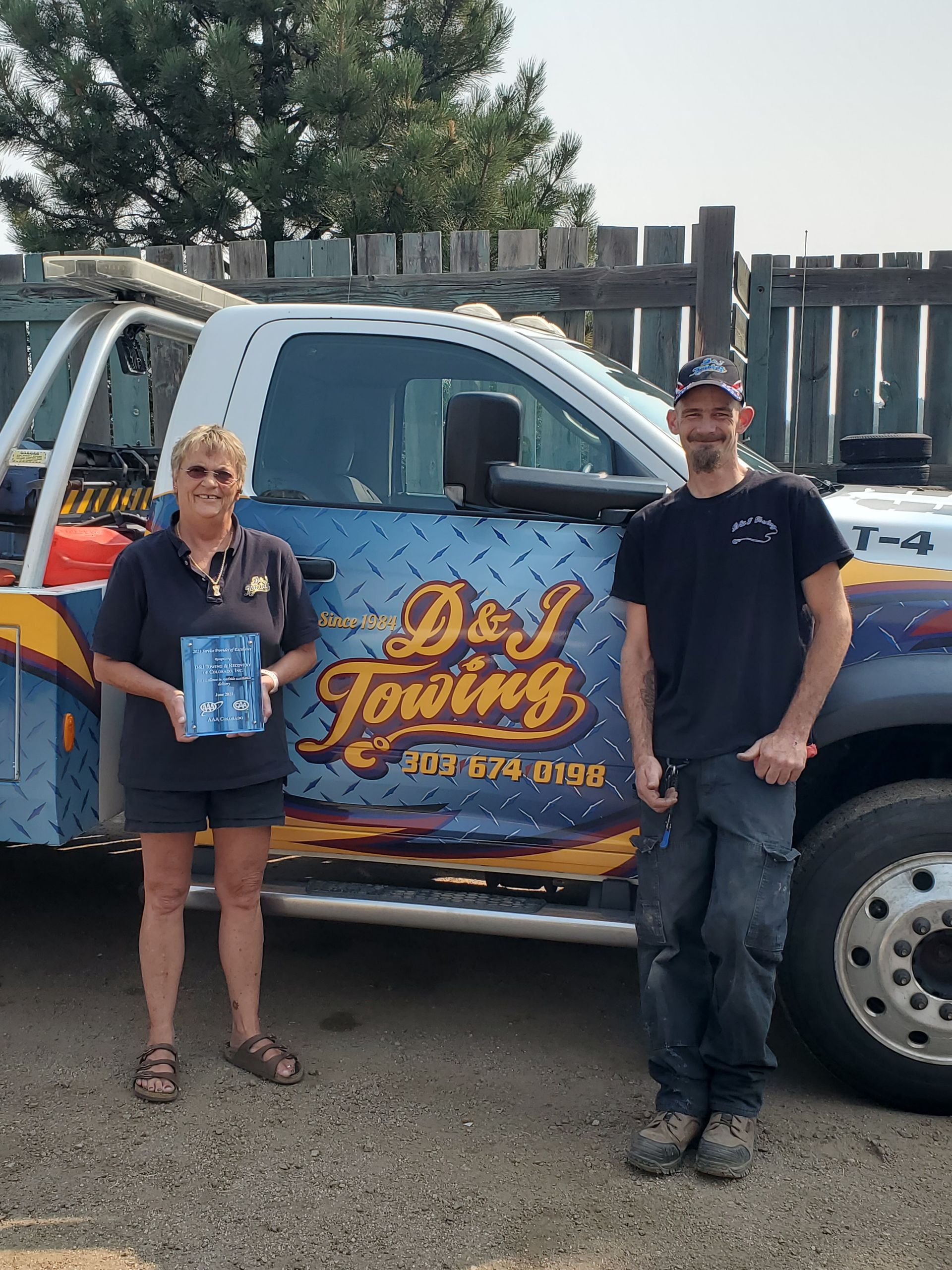 A man and a woman are standing in front of a towing truck.