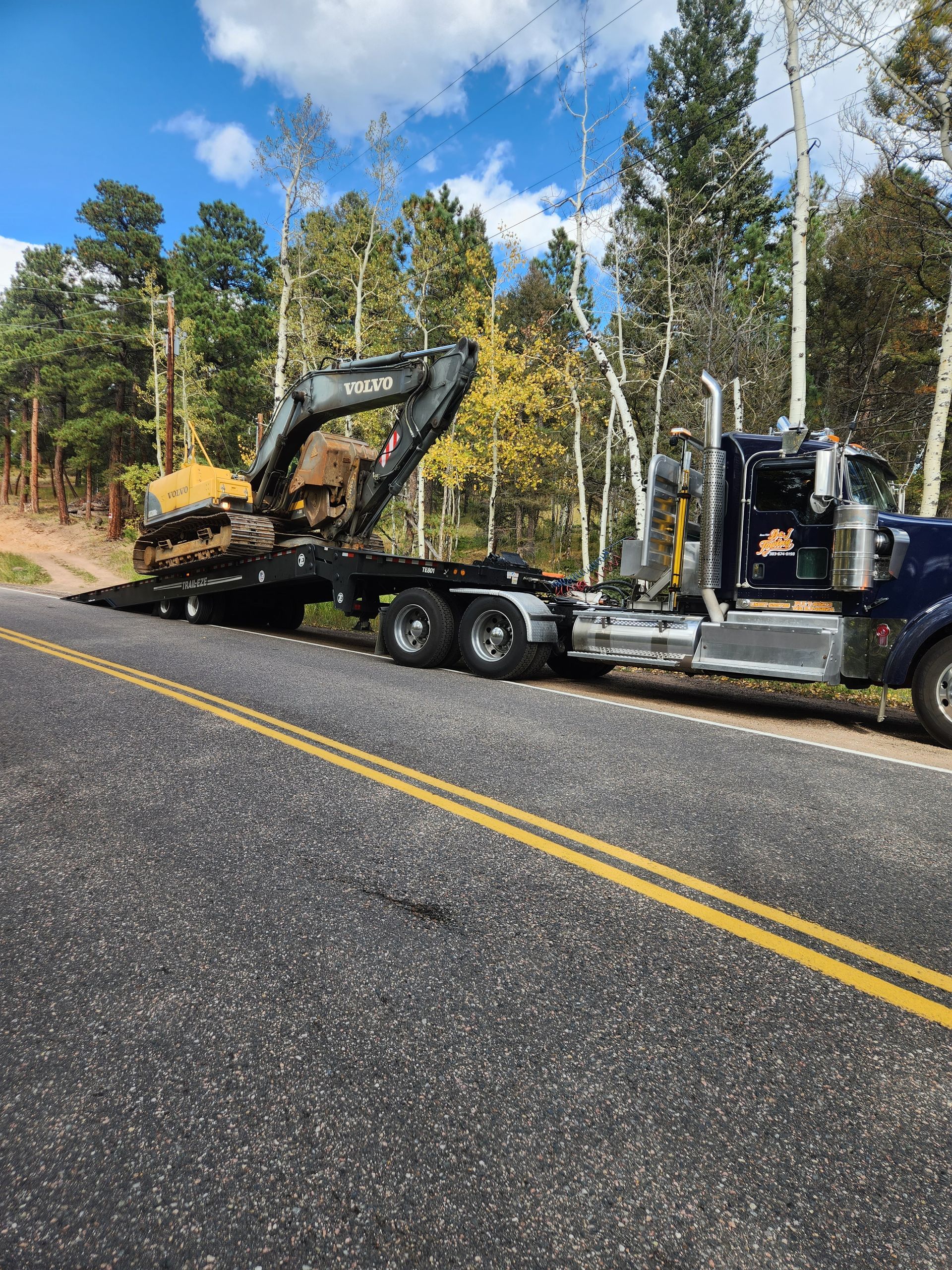 A semi truck is carrying a large excavator down a road.