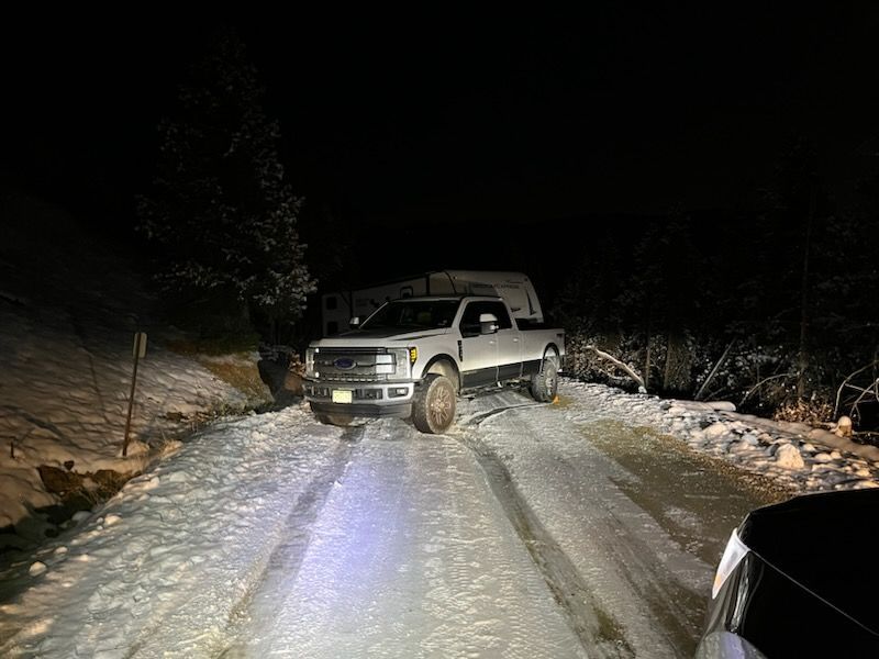 A white truck is driving down a snowy road at night.