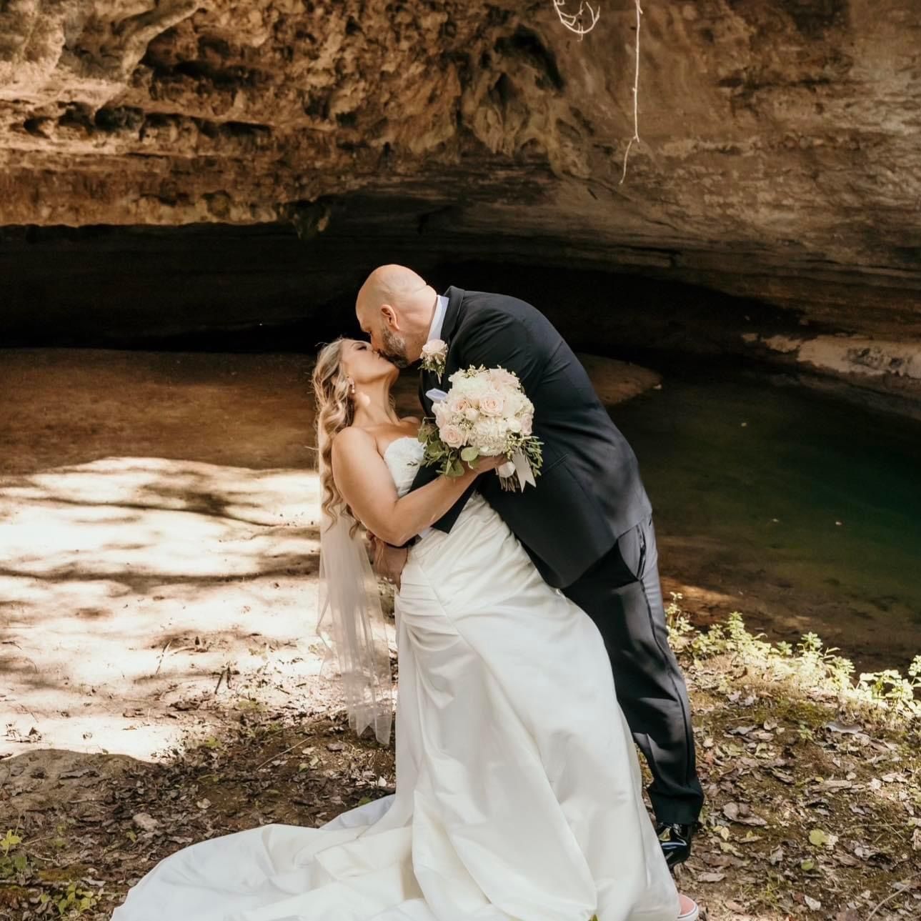 A bride and groom kissing in front of a cave.