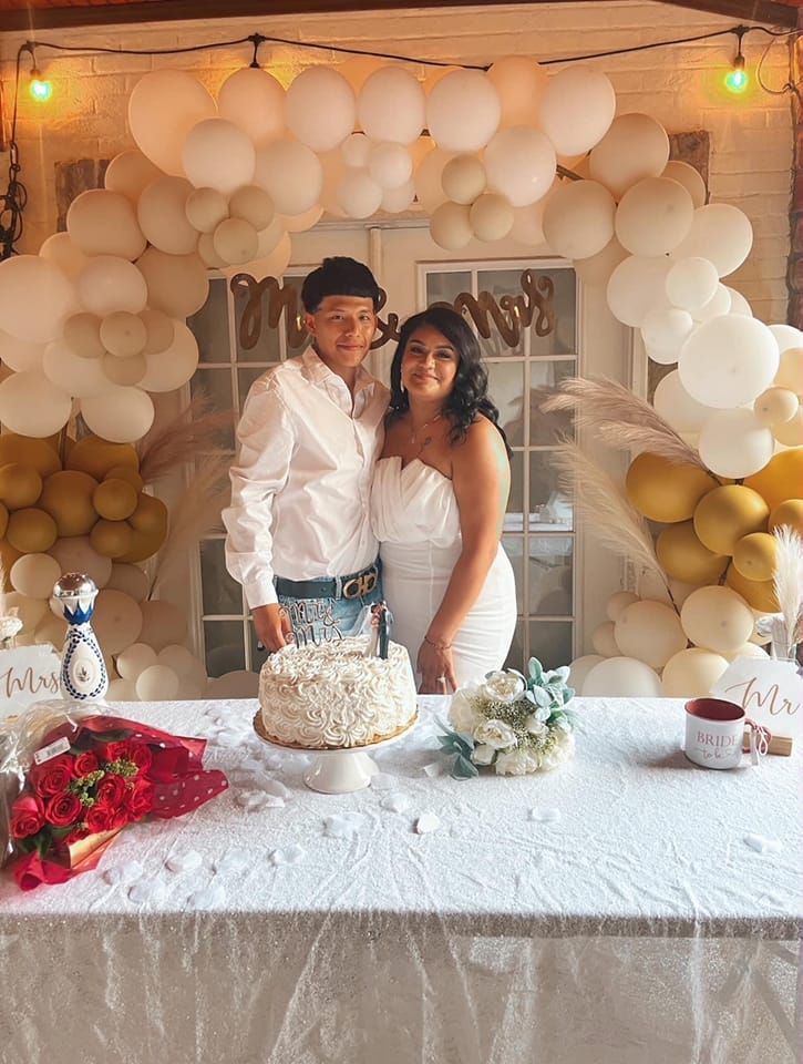 A man and woman are standing in front of a table with a cake and balloons.