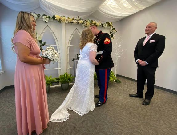 A bride and groom are getting married in a small room while a man in a suit stands behind them.