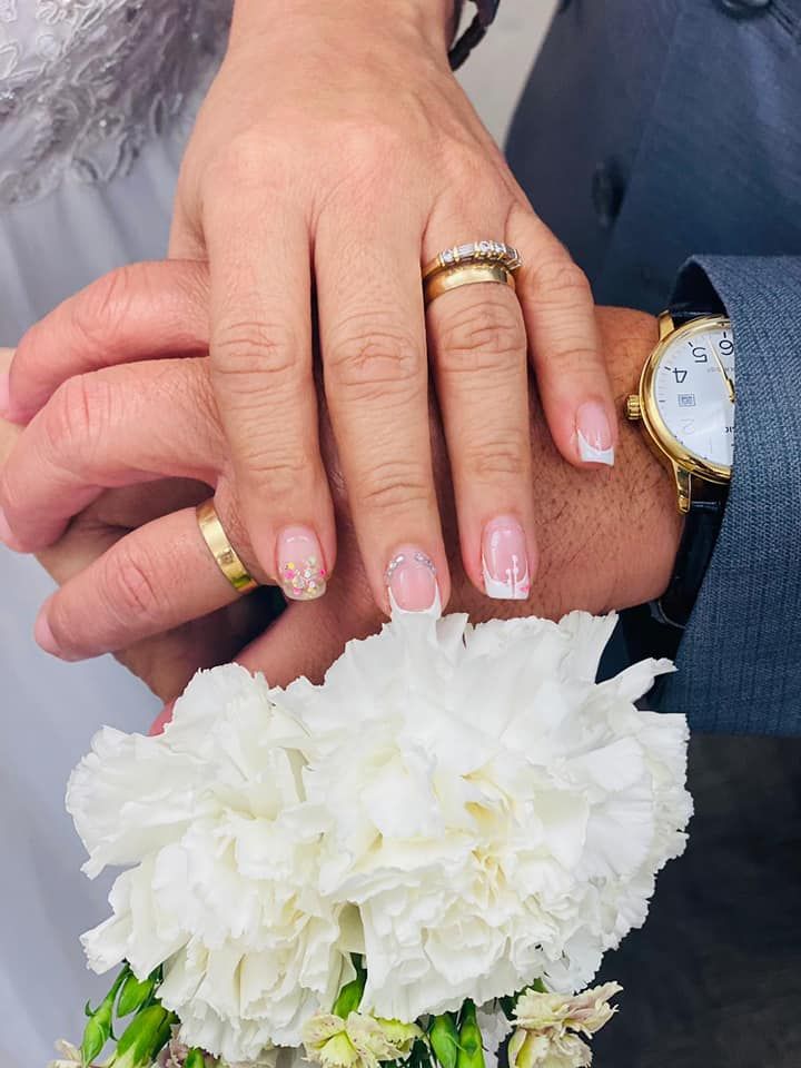 The bride and groom are wearing wedding rings and holding a bouquet of white flowers.