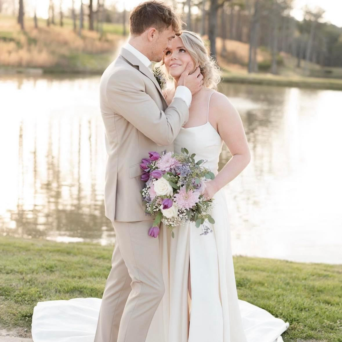 A bride and groom are posing for a picture in front of a lake.