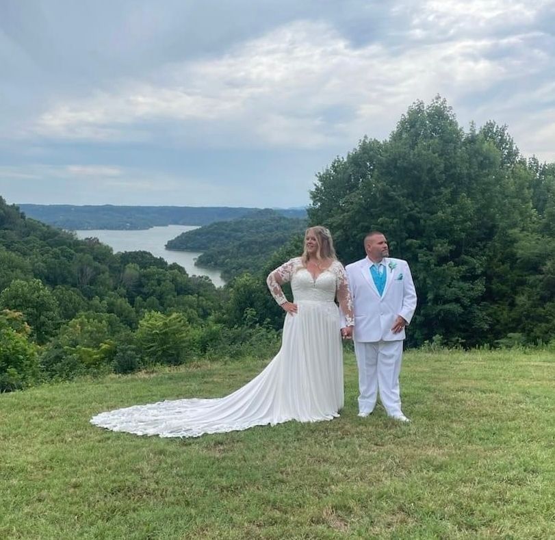 A bride and groom are posing for a picture in a field with a lake in the background.