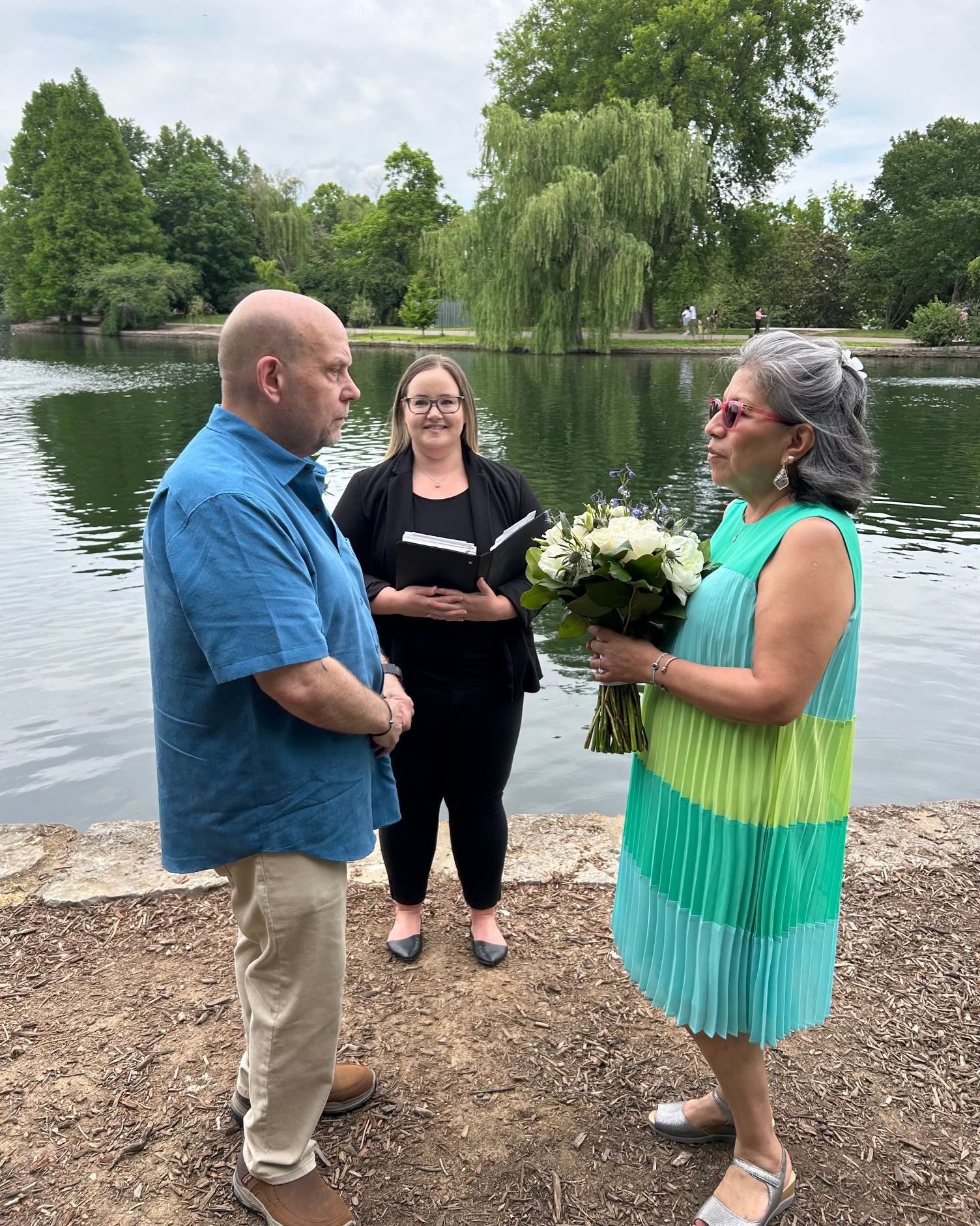 A man and a woman are standing next to each other in front of a lake.