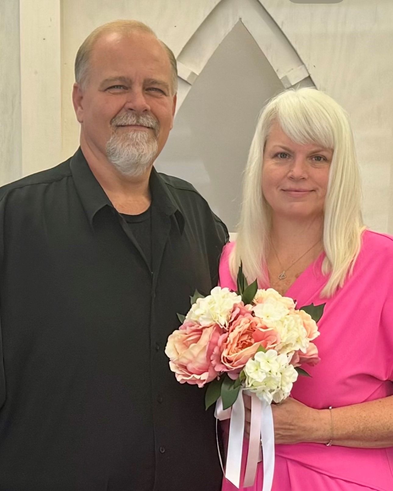 A man and a woman are posing for a picture while the woman is holding a bouquet of flowers.