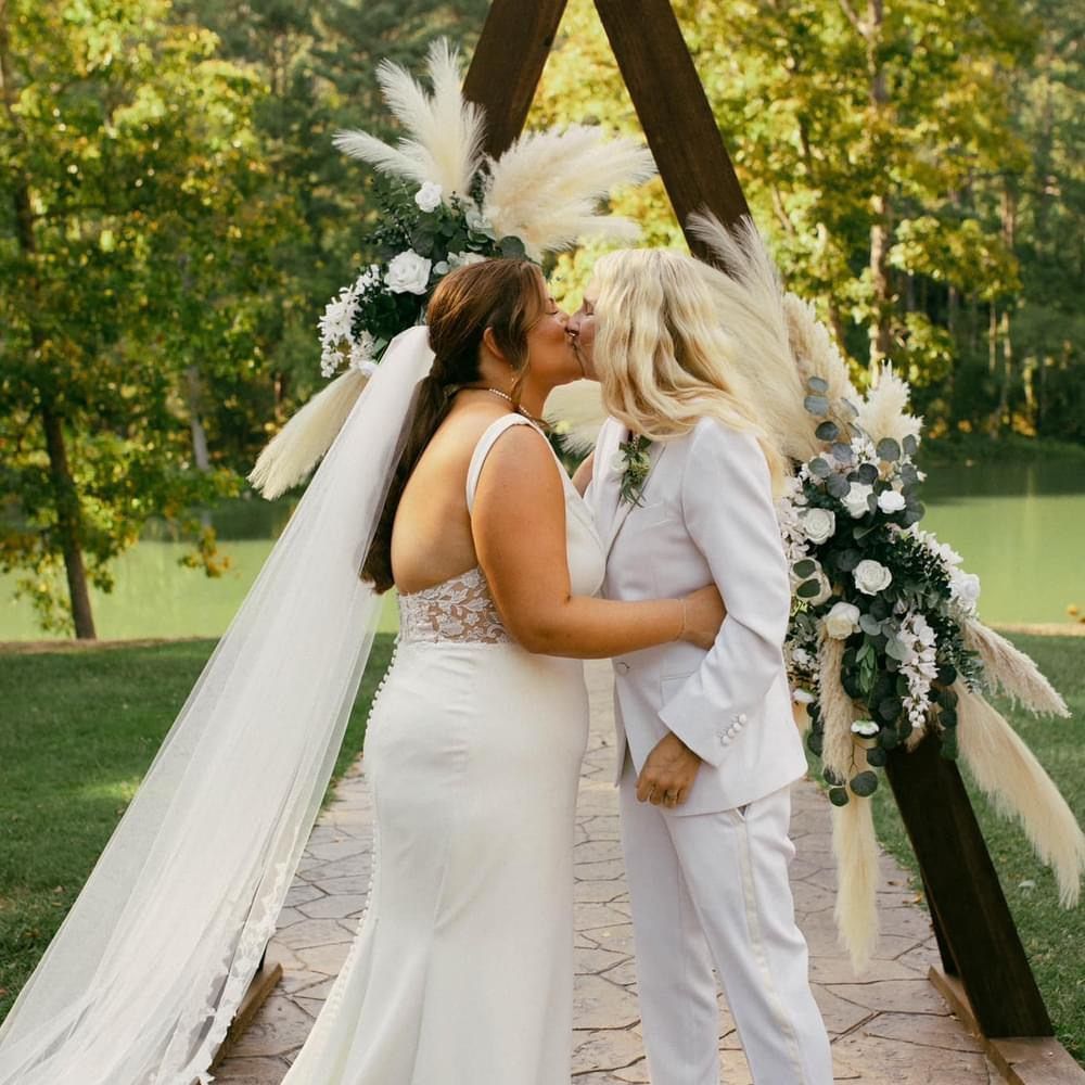 A bride and groom kissing under a wooden arch.