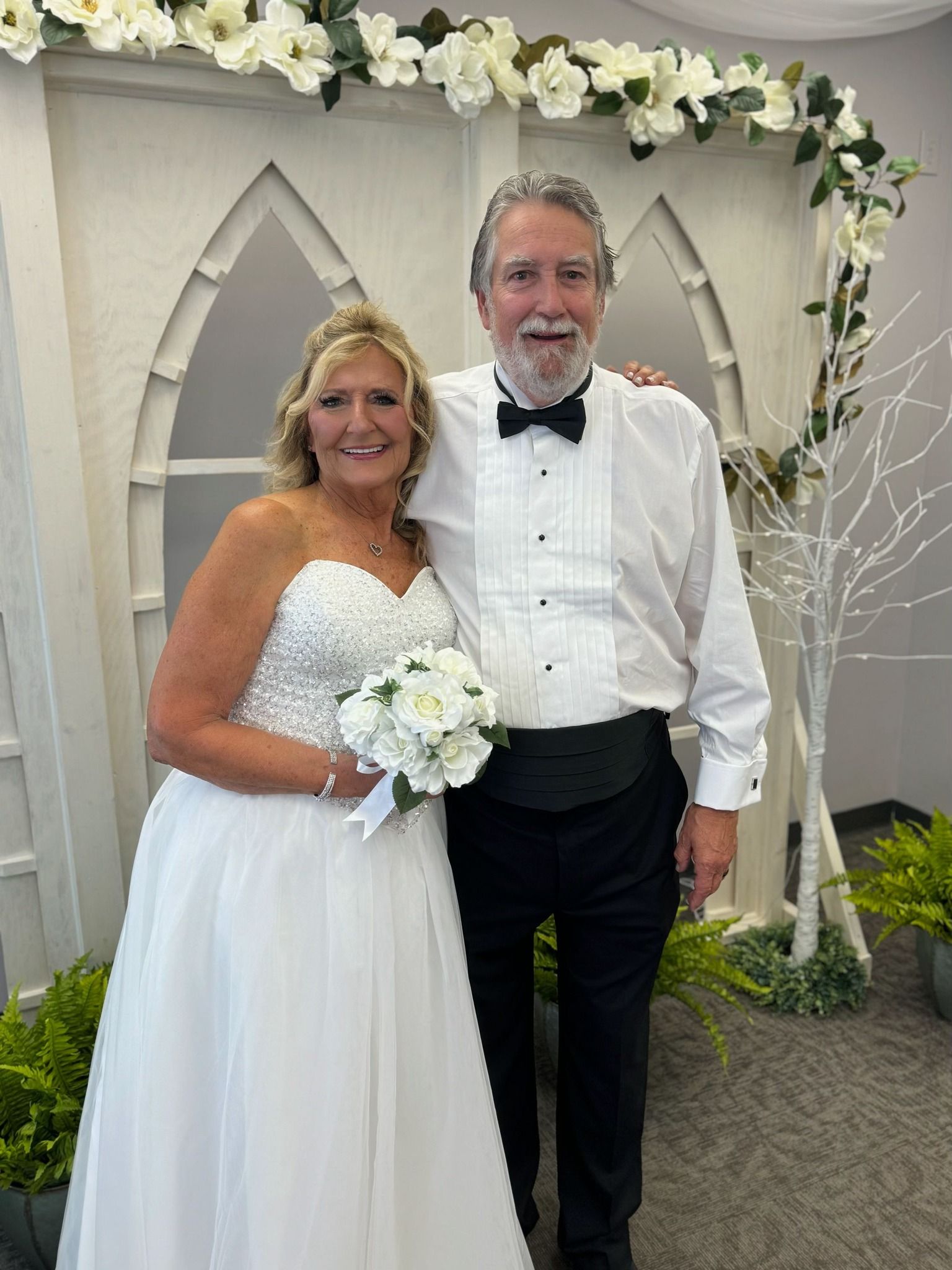 A bride and groom are posing for a picture in front of a white arch.