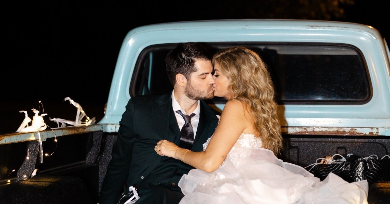 A bride and groom are kissing in the back of a truck.