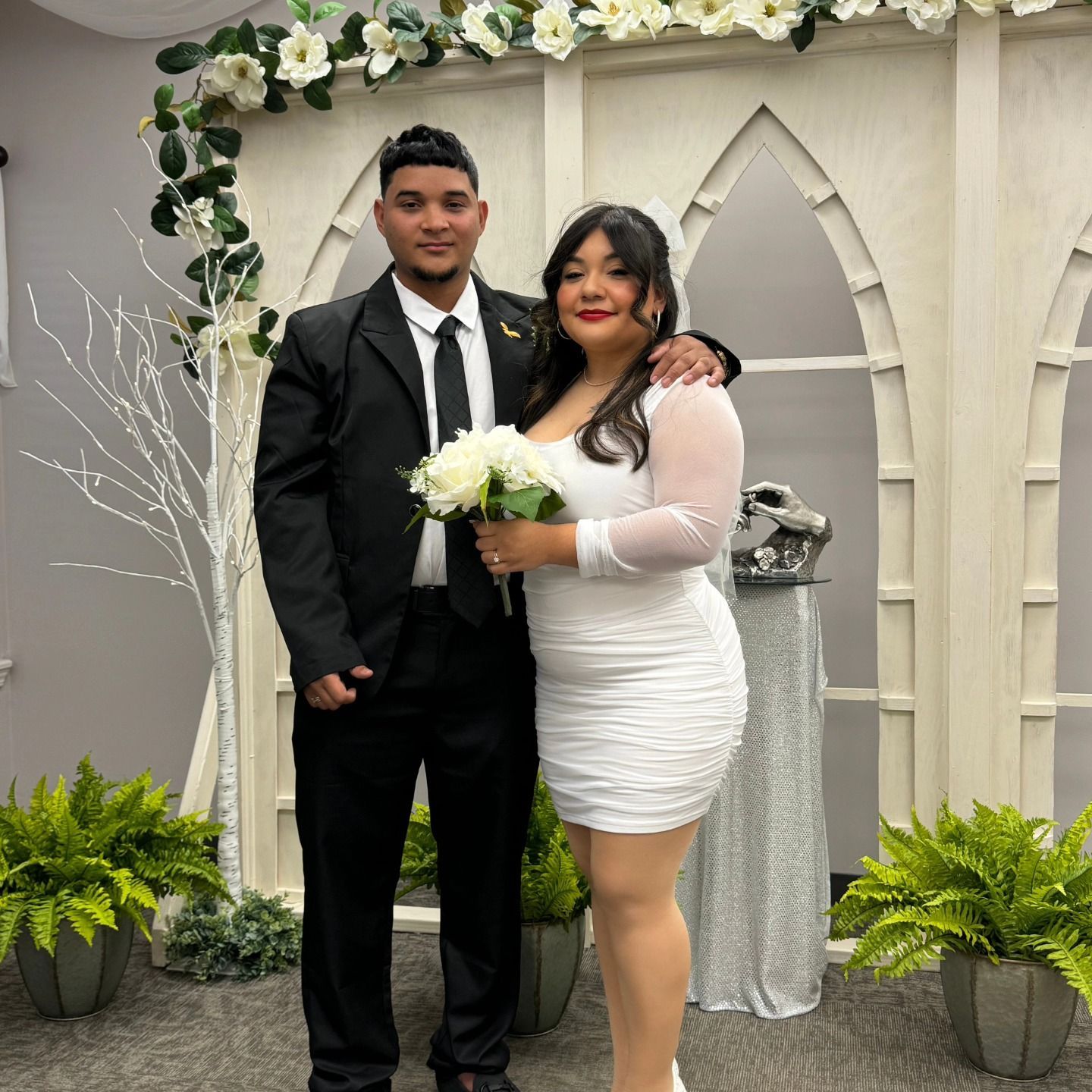 A bride and groom are posing for a picture in front of a flower arch.